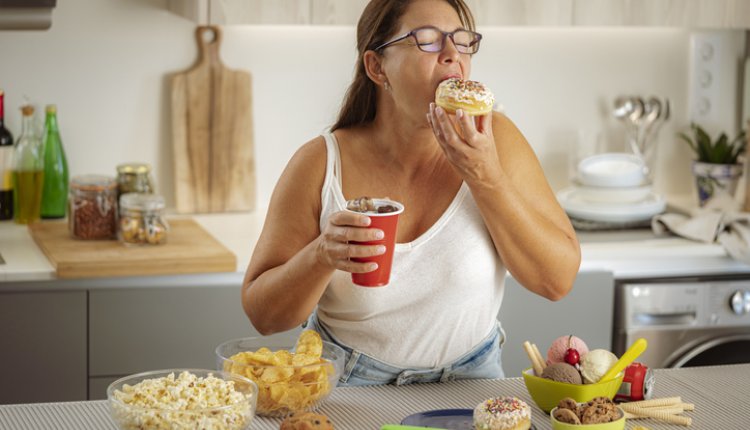 Ultra processed foods zoals chips, donuts, frisdrank, koek en ijs. Vrouw smult van sterk bewerkt voedsel