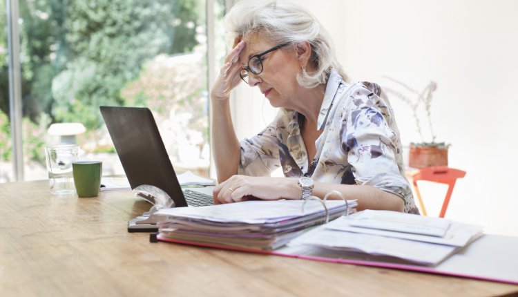 oudere dame aan het werk achter een laptop met veel papierwerk