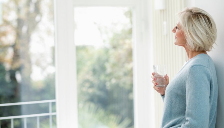 Vrouw drinkt glas water en kijkt nadenkend uit het raam