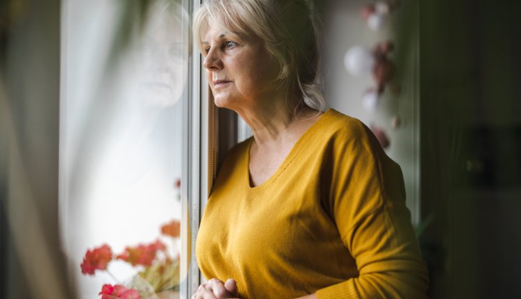 Oudere vrouw kijkt mistroostig uit het raam