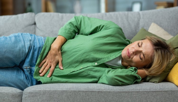 Norovirus buikpijn vrouw ligt op de bank met handen op buik