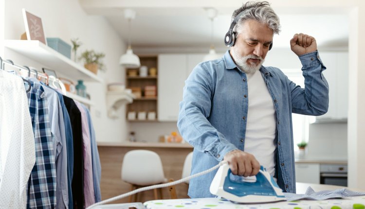 Oudere man is enthousiast aan het strijken met muziek aan