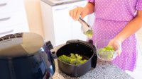 Vrouw in roze jurk doet broccoli in airfryer