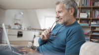 Oudere man checkt email op zijn laptop in de woonkamer met boekenkast