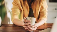 Vrouw zit aan tafel met kop koffie voor zich