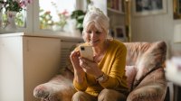 Vrouw met smartphone bezig in de woonkamer, zittend op stoel