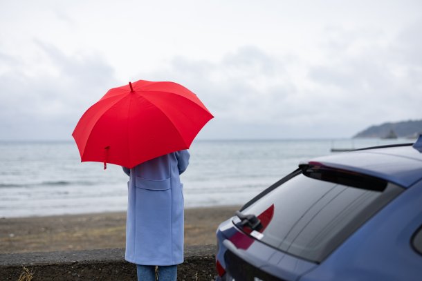 Regen vrouw met paraplu met auto aan het strand