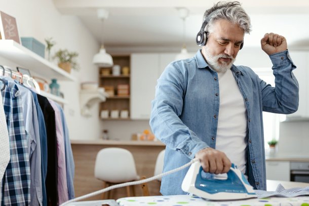 Oudere man is enthousiast aan het strijken met muziek aan